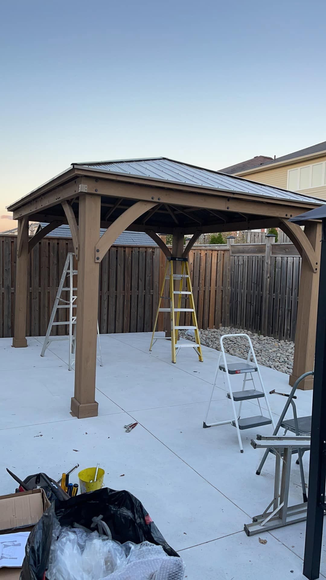 Gazebo mid-assembly on a new concrete patio with ladders set up